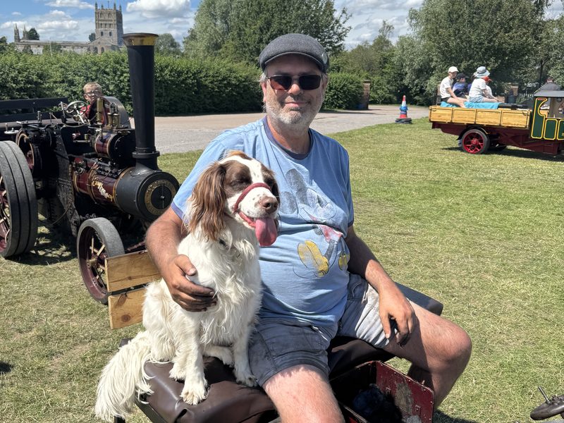 Nellie's driver relaxing beside the engine with his springer spaniel at a rally, Tewkesbury Abbey on the skyline